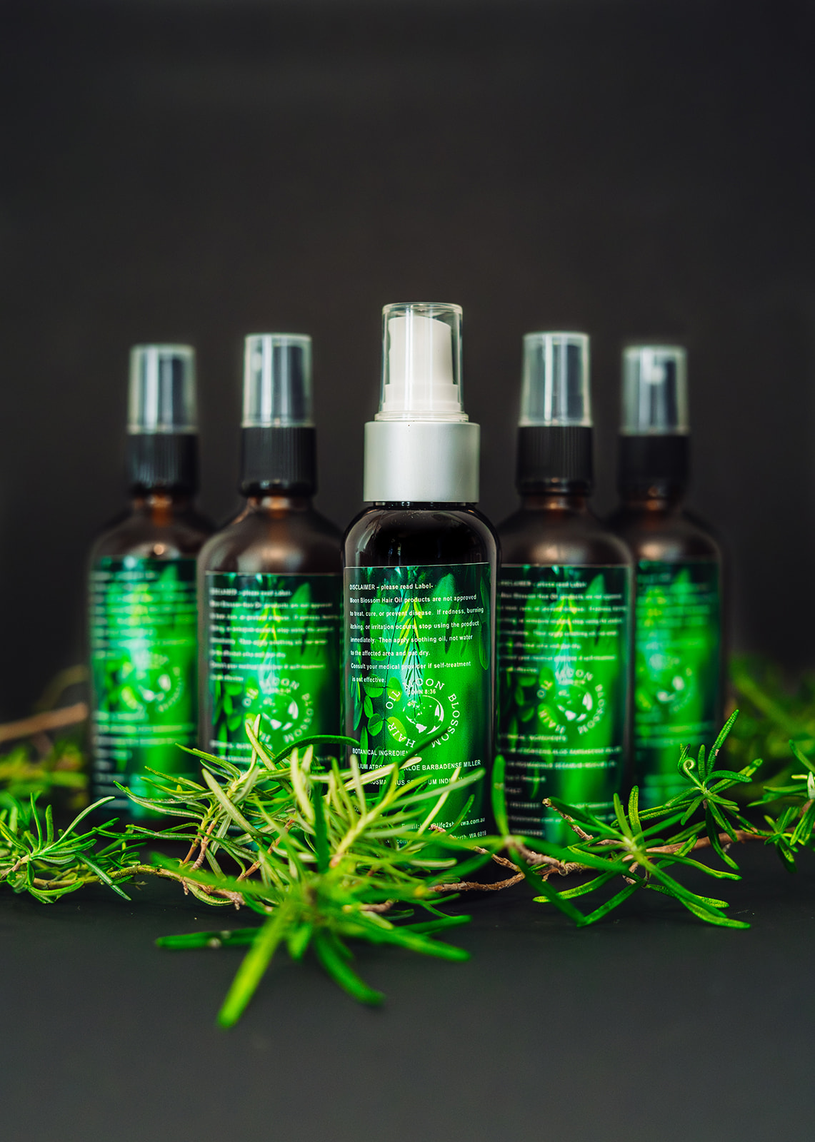 Moon Blossom Hair Oil amber spray bottles surrounded by fresh rosemary